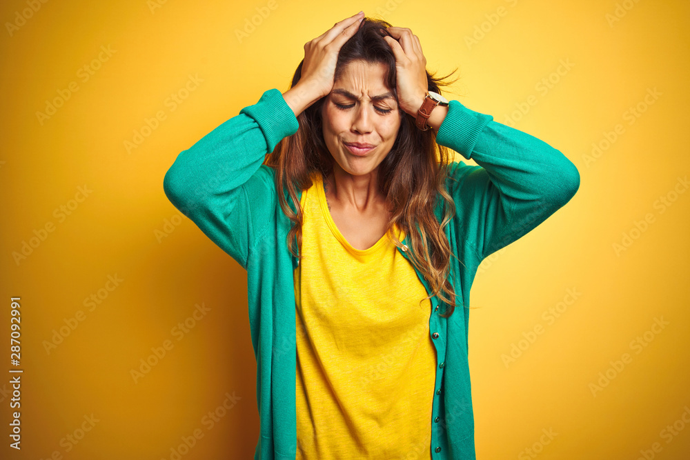 Young woman wearing t-shirt and green sweater standing over yelllow isolated background suffering from headache desperate and stressed because pain and migraine. Hands on head. Young woman wearing t-shirt and green sweater standing over yelllow isolated background suffering from headache desperate and stressed because pain and migraine. Hands on head.