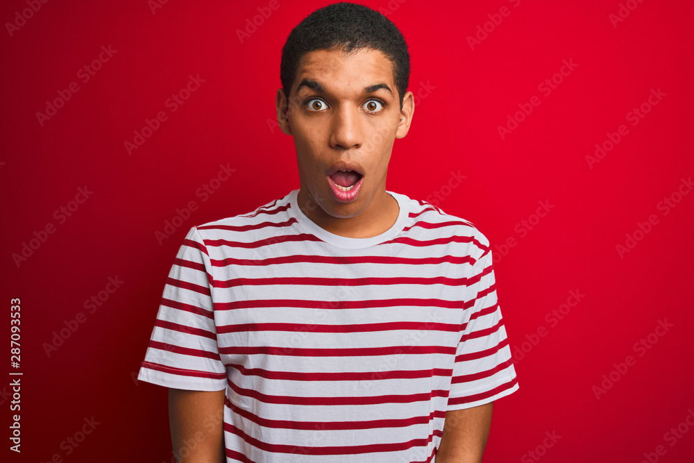 Young handsome arab man wearing striped t-shirt over isolated red background afraid and shocked with surprise and amazed expression, fear and excited face. Young handsome arab man wearing striped t-shirt over isolated red background afraid and shocked with surprise and amazed expression, fear and excited face.