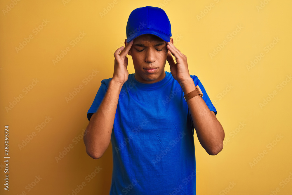Young handsome arab delivery man standing over isolated yellow background with hand on head for pain in head because stress. Suffering migraine.