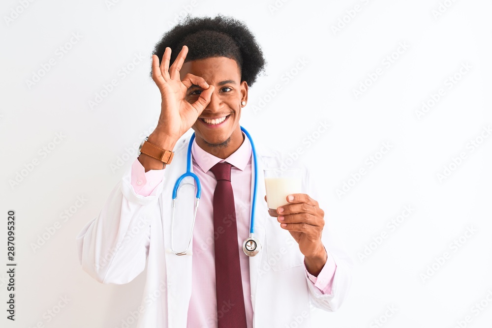 Young african american doctor man drinking glass of milk over isolated white background with happy face smiling doing ok sign with hand on eye looking through fingers