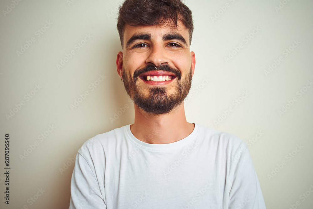 Fototapeta premium Young man with tattoo wearing t-shirt standing over isolated white background happy face smiling with crossed arms looking at the camera. Positive person.