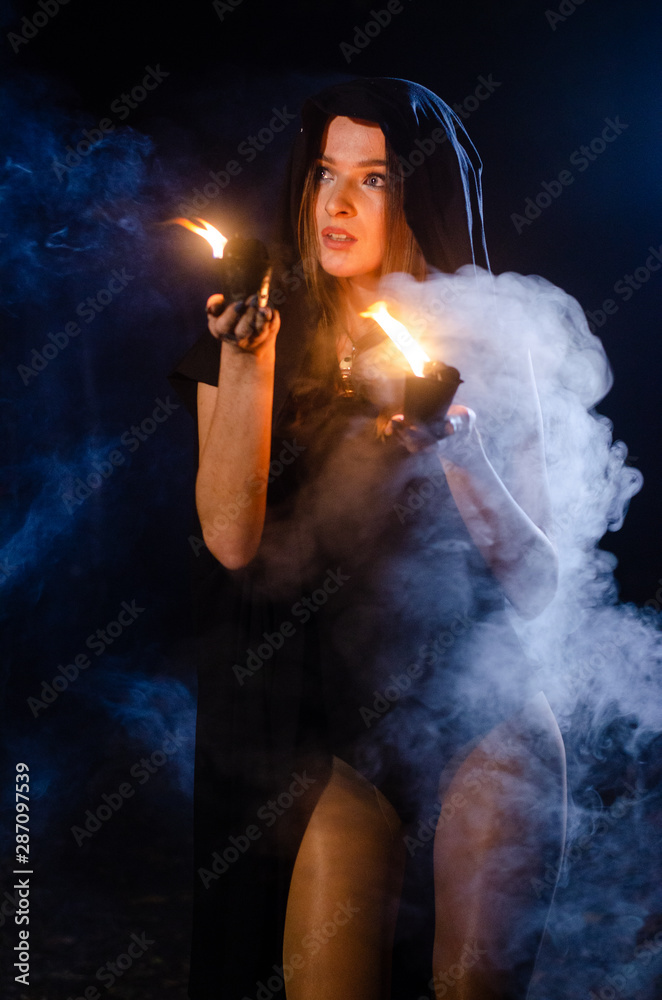 Young girl in a long black coat fire night.