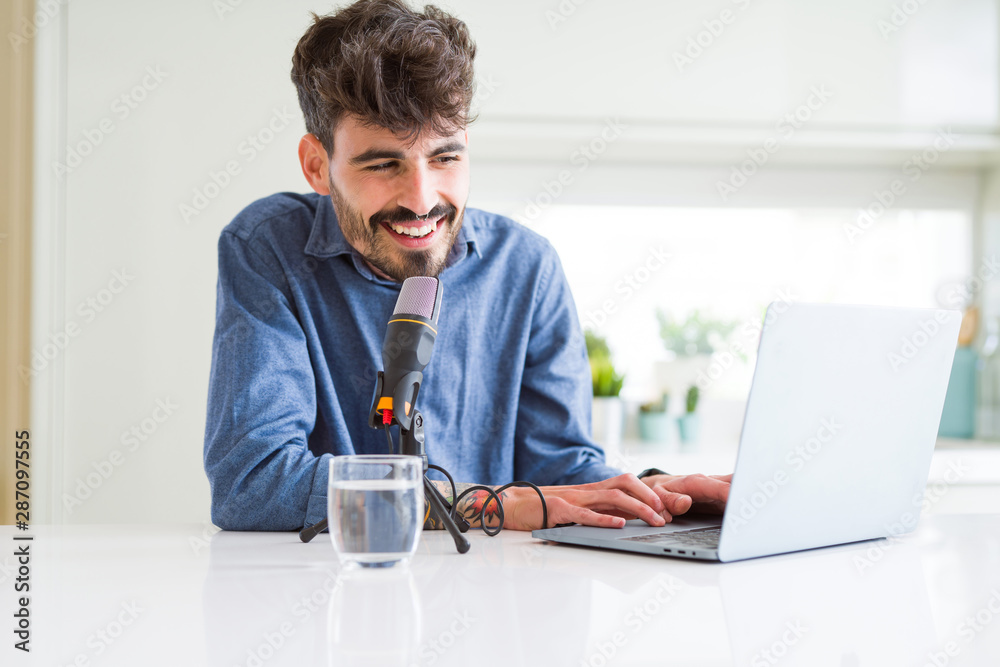 Young hipster man recording podcast using laptop, broadcasting an interview using microphone Young hipster man recording podcast using laptop, broadcasting an interview using microphone