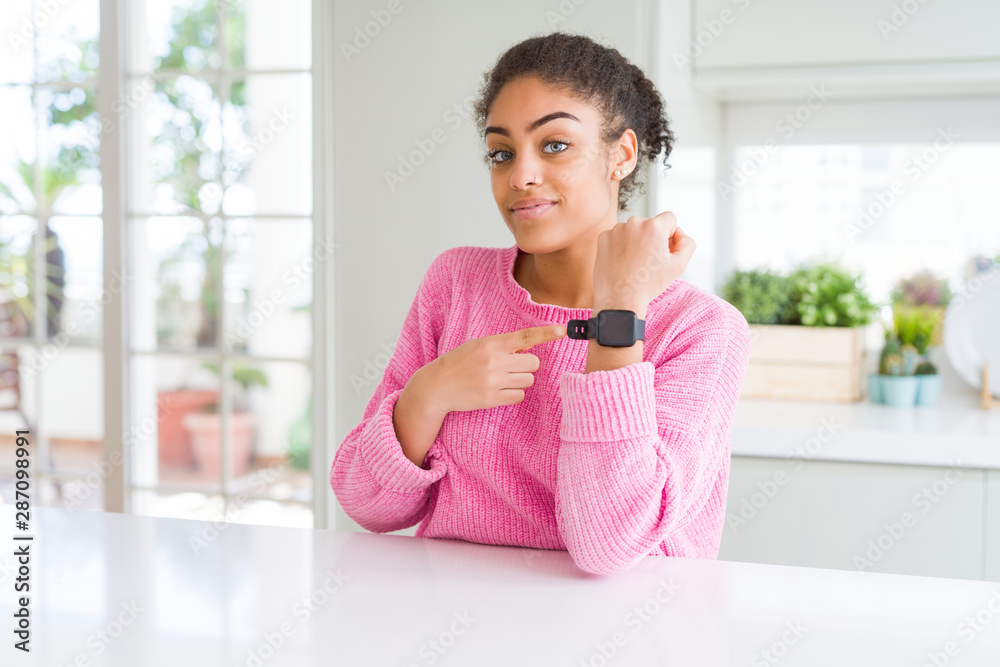 Beautiful african american woman with afro hair wearing casual pink sweater In hurry pointing to watch time, impatience, looking at the camera with relaxed expression Beautiful african american woman with afro hair wearing casual pink sweater In hurry pointing to watch time, impatience, looking at the camera with relaxed expression