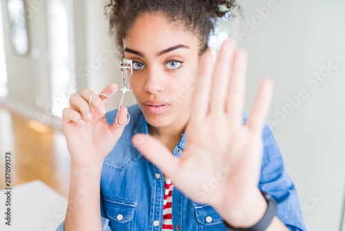 Young african american girl using eyelashes curler with open hand doing stop sign with serious and confident expression, defense gesture