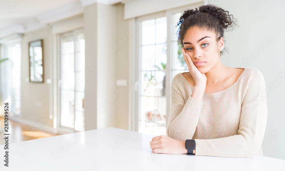 Beautiful young african american woman with afro hair sitting on table at home thinking looking tired and bored with depression problems with crossed arms. Beautiful young african american woman with afro hair sitting on table at home thinking looking tired and bored with depression problems with crossed arms.