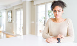 Beautiful young african american woman with afro hair sitting on table at home depressed and worry for distress, crying angry and afraid. Sad expression.