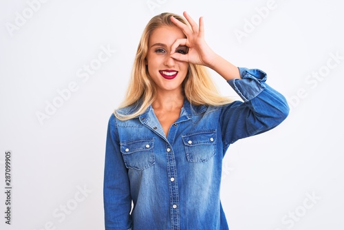 Young beautiful woman wearing casual denim shirt standing over isolated white background doing ok gesture with hand smiling, eye looking through fingers with happy face.