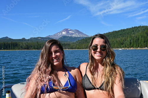 Two young women on boat in Elk Lake, Oregon with South Sister volcano in background on sunny summer afternoon.