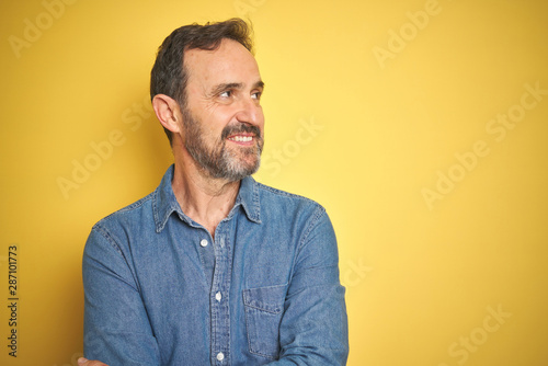 Handsome middle age senior man with grey hair over isolated yellow background smiling looking to the side and staring away thinking.