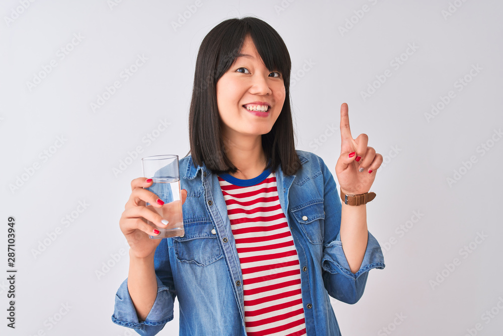 Young beautiful Chinese woman holding glass of water over isolated white background surprised with an idea or question pointing finger with happy face, number one Young beautiful Chinese woman holding glass of water over isolated white background surprised with an idea or question pointing finger with happy face, number one