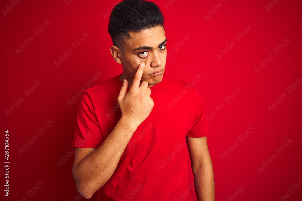 Young brazilian man wearing t-shirt standing over isolated red background Pointing to the eye watching you gesture, suspicious expression Young brazilian man wearing t-shirt standing over isolated red background Pointing to the eye watching you gesture, suspicious expression