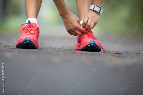 Young woman trail runner tying shoelaces in forest