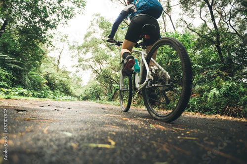 Woman cyclist riding mountain bike on tropical rainforest trail photo