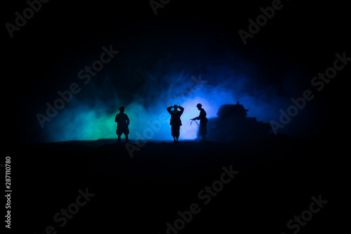 Battle scene. Military silhouettes fighting scene on war fog sky background. A German soldiers raised arms to surrender. Plastic toy soldiers with guns taking prisoner the enemy soldier.