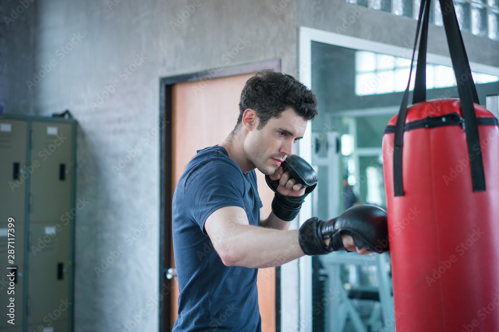 Handsome man in boxing gloves punching bags exercise in fitness gym