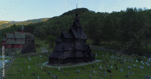 Aerial: Drone moving around tombstones surrounding Kaupanger Stave Church by trees photo