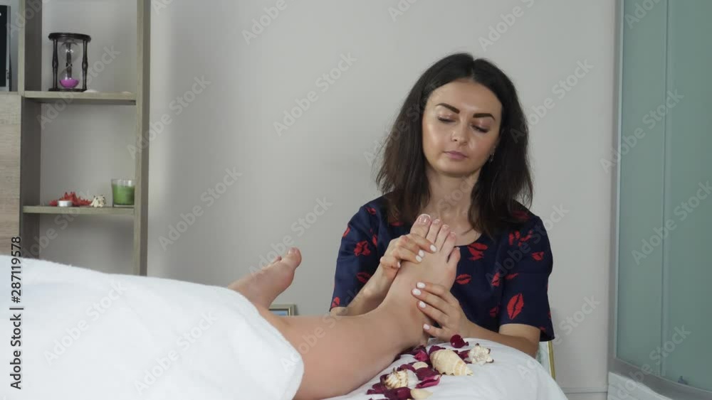Female masseur massaging feet in spa salon. Woman in therapy room lying on bed with rose petals. Thai massage Female masseur massaging feet in spa salon. Woman in therapy room lying on bed with rose petals. Thai massage