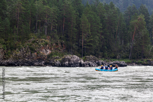 A team of athletes in a blue inflatable boat rafts down a mountain river amid a green forest and mountains.rafting on a mountain river