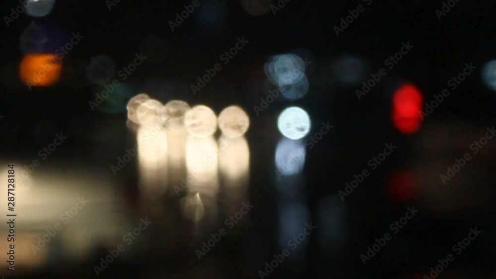 Rain water drops Falling Down On the Windscreen in slow motion, Rain Drops On The Windows Glass, Defocused Night City Traffic Lights. Color Blurred bokeh of moving transport and typical city noise. Rain water drops Falling Down On the Windscreen in slow motion, Rain Drops On The Windows Glass, Defocused Night City Traffic Lights. Color Blurred bokeh of moving transport and typical city noise.
