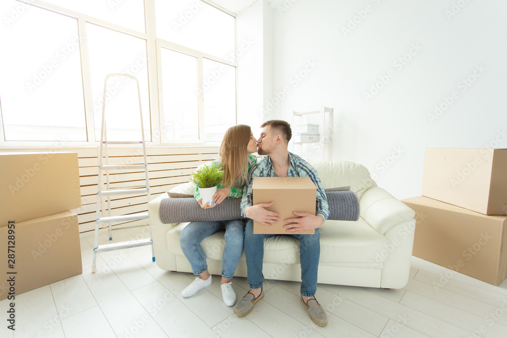 Moving and real estate concept - Happy couple kissing on sofa in their new flat Moving and real estate concept - Happy couple kissing on sofa in their new flat