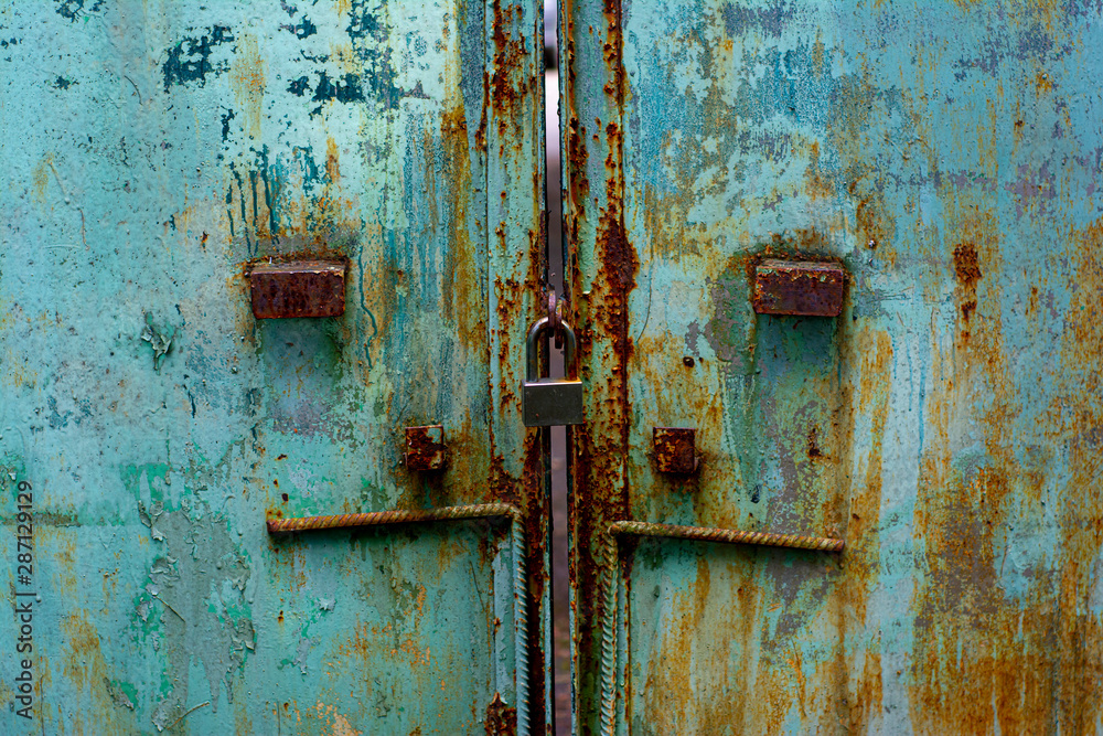 The texture of the old metal gate painted in blue-green color with large stains of rust and a lock The texture of the old metal gate painted in blue-green color with large stains of rust and a lock