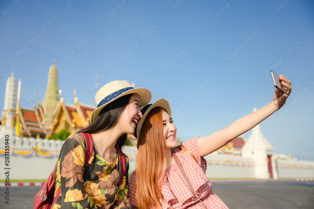young tourist women enjoy traveling in sitting selfie picture in front of the palace temple in Bangkok of Thailand, Emerald Buddha Temple, Wat Phra Kaew, Bangkok Royal Palace popular tourist place