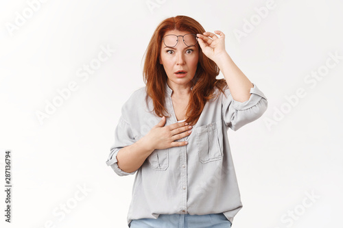 Oh gosh what happened. Worried speechless stunned redhead middle-aged mother take-off glasses panic hold hand heart open mouth gasping nervously react shook intense stare camera white background