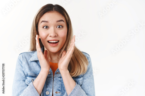 Close-up excited surprised impressed asian blond girl wondering amused stare camera open mouth broad toothy smile stunned touch gace astonished awesome news happy reaction white wall