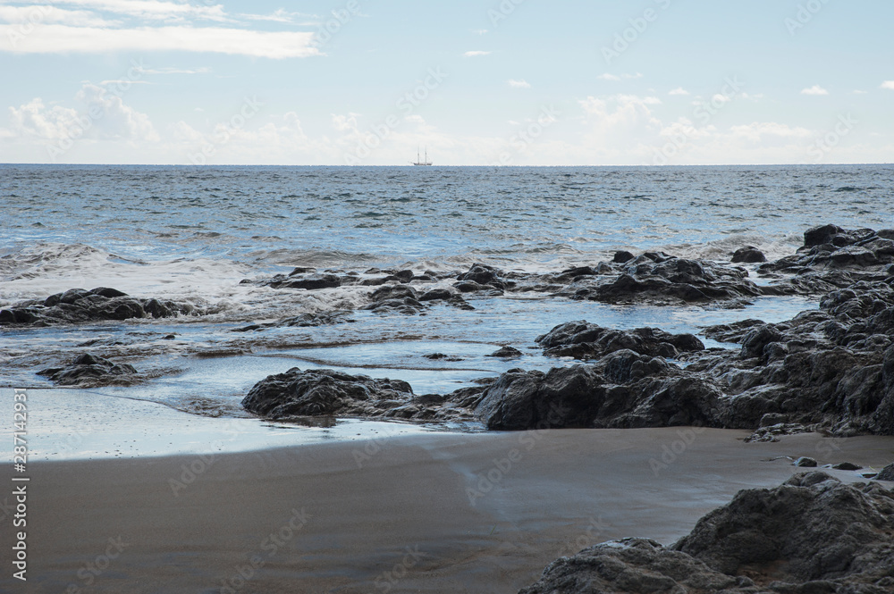 Fototapeta premium View of a beautiful remote volcanic sand beach with tranquil waves hitting rocks and sand, on a cloudy day, after the storm, on the northern coast of the island of Tenerife, Canary Islands, Spain