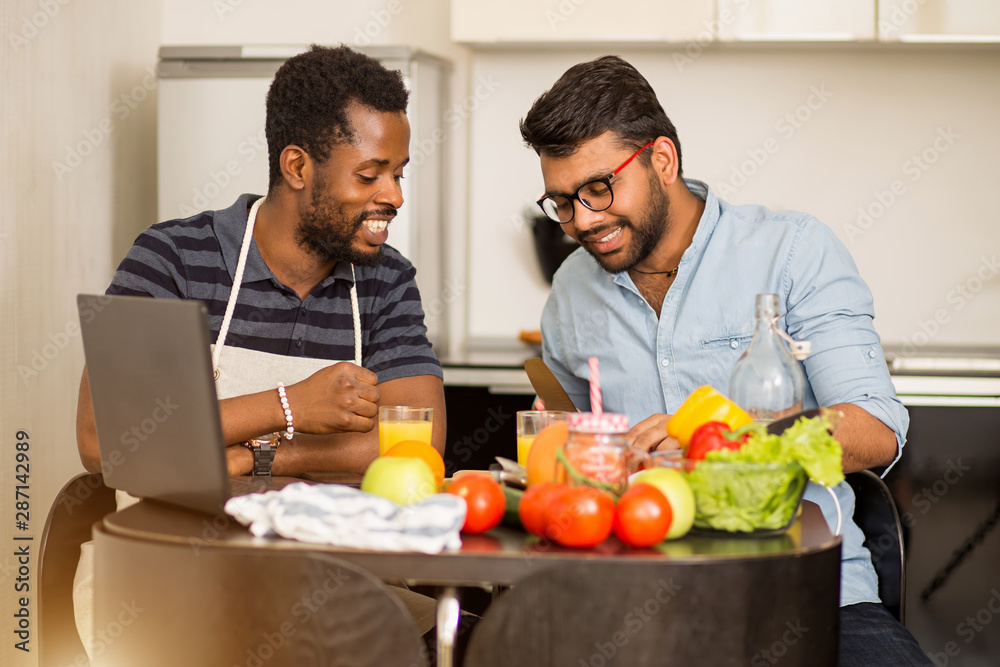 Two men using laptop in kitchen Two men using laptop in kitchen