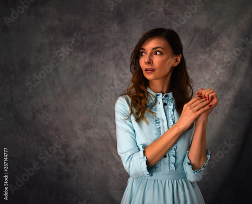 Young brunette girl in blue dress looks away on background.