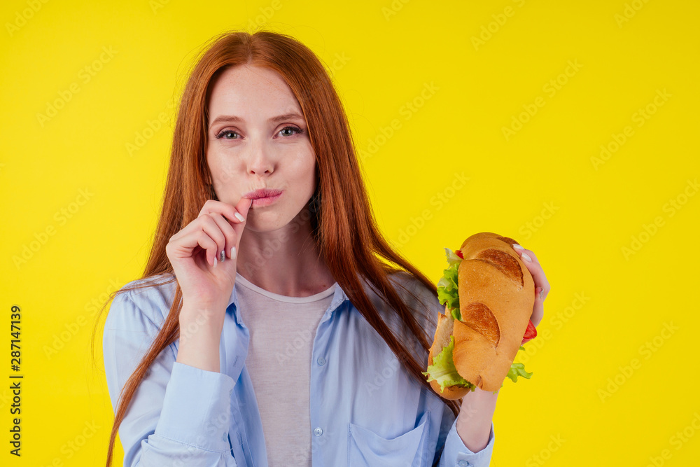 beautiful redhaired ginger woman real jam licking fingers holding huge sandwich Titanic in studio yellow background