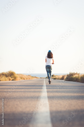 Woman riding an electric kick scooter on a lonely road