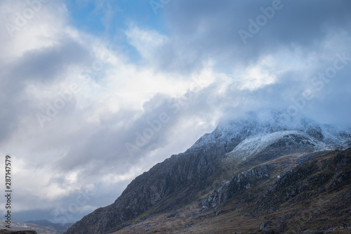 Stunning moody dramatic Winter landscape image of snowcapped Tryfan mountain in Snowdonia with stormy weather brooding overhead