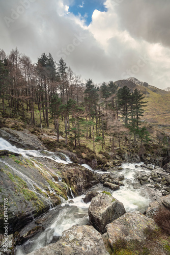 Stunning landscape image of Ogwen Valley river and waterfalls during Winter with snowcapped mountains in background