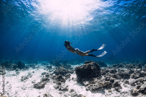 Free diver woman with fins glides over corals in blue sea.