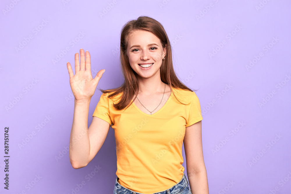 Image of friendly pretty teenager girl saying hi to new classmates, happy to make new friends, feels positive emotions, glad to be fresh comer, looks in camera with wide smile, dressed casually.