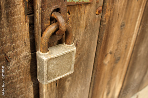 Old rusty squre padlock hanging on brown wooden door