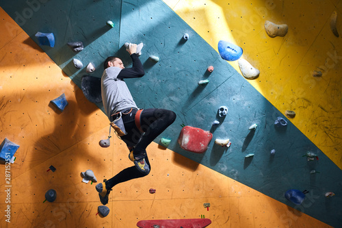 Young athletic sportsman has dynamic training in bouldering gym, runs out of energy, feels tired and exhausted, needs some break and rest, climbing down from artificial rock wall.