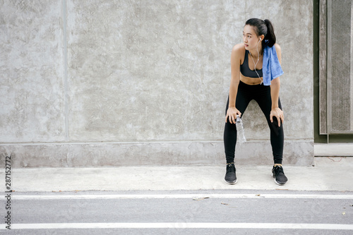 Young asian woman runner resting after workout running in street city road.