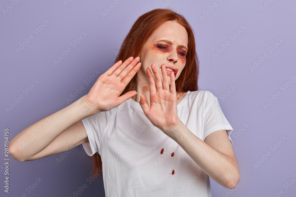 Stop hurting women Young beaten up scared ginger woman with closed eyes stretching out hand while standing against blue wall. fear. fobia. Don't touch me Stop hurting women Young beaten up scared ginger woman with closed eyes stretching out hand while standing against blue wall. fear. fobia. Don't touch me