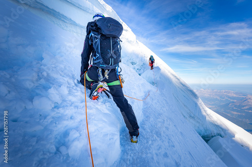 Two alpinists mountaineers climbing over ice crevasse.