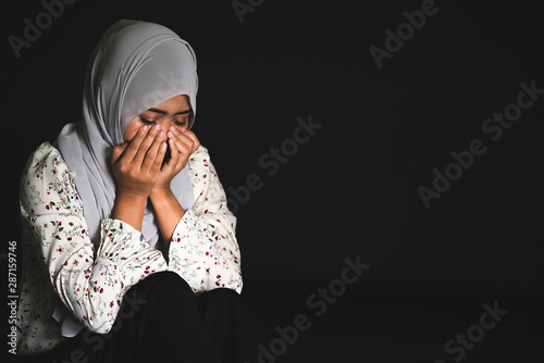 Young Muslim girl sitting in dark room feeling pain with life problem. Crying muslim female holding painful hand, suffering from husband violence