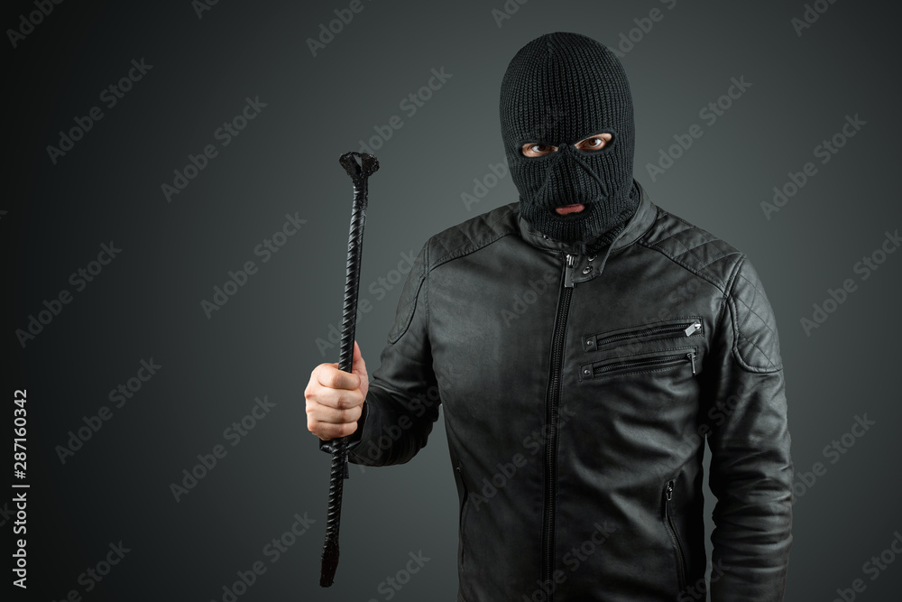Robber, bandit in a balaclava with a crowbar in his hands on a black background. Robbery, hacker, crime, theft. Copy space. Robber, bandit in a balaclava with a crowbar in his hands on a black background. Robbery, hacker, crime, theft. Copy space.