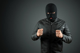Robber, thug in a balaclava on a black background. Robbery, hacker, crime, theft. Copy space.