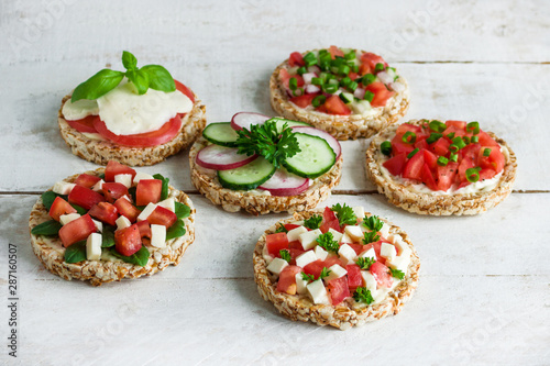 rice crisp cracker with chopped vegetables tomato cucumber radish parsley soft cheese on white wooden table