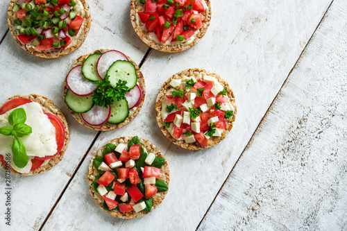 healthy open sandwiches with rice cake chopped tomatoes radish cucumber basil cheese green onion on white wooden background top view copy space