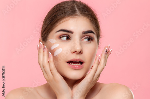 Happy beautiful model isolated over pink background. Moisturizing hyaluronic cream applied to skin. Concept of beauty and health treatment.