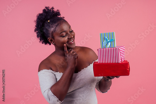 happy afro woman holding gift boxes March 8 in stusio pink background photo